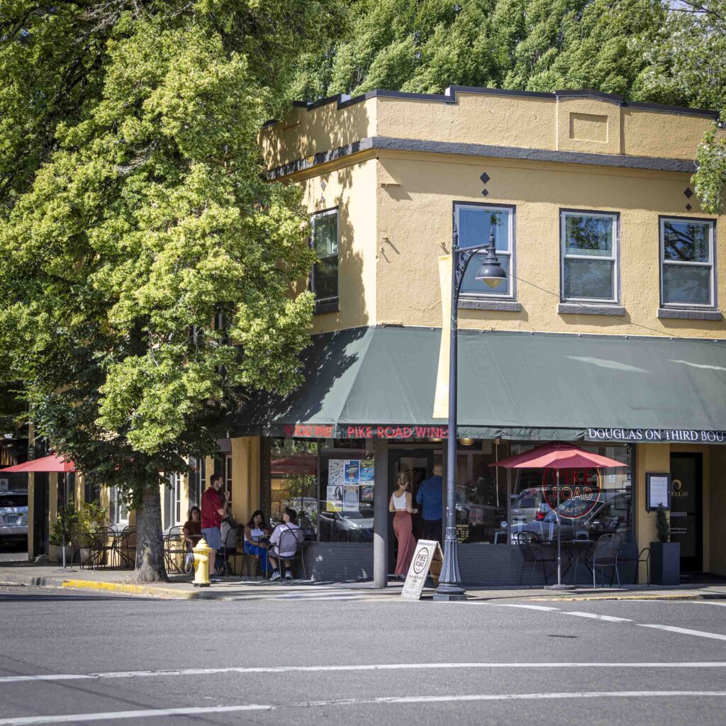 Exterior of a yellow two story building with green awnings and people drinking wine outside