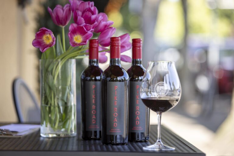 Three bottles of red wine and a glass of wine on an outdoor table with pink tulips